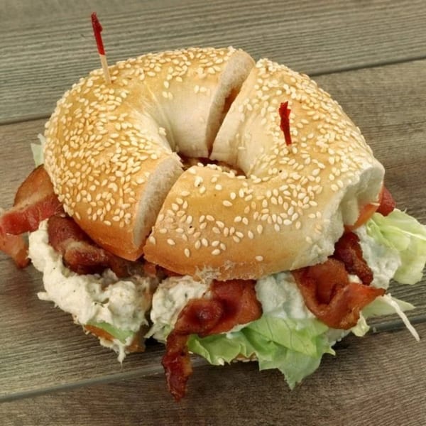 A sesame bagel with bacon, lettuce, and cream cheese, cut in half with toothpicks, on a wooden surface.