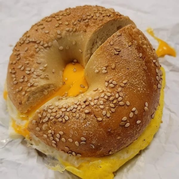A sesame bagel from The Bagel Club, sliced open with a fried egg and melted cheese inside.