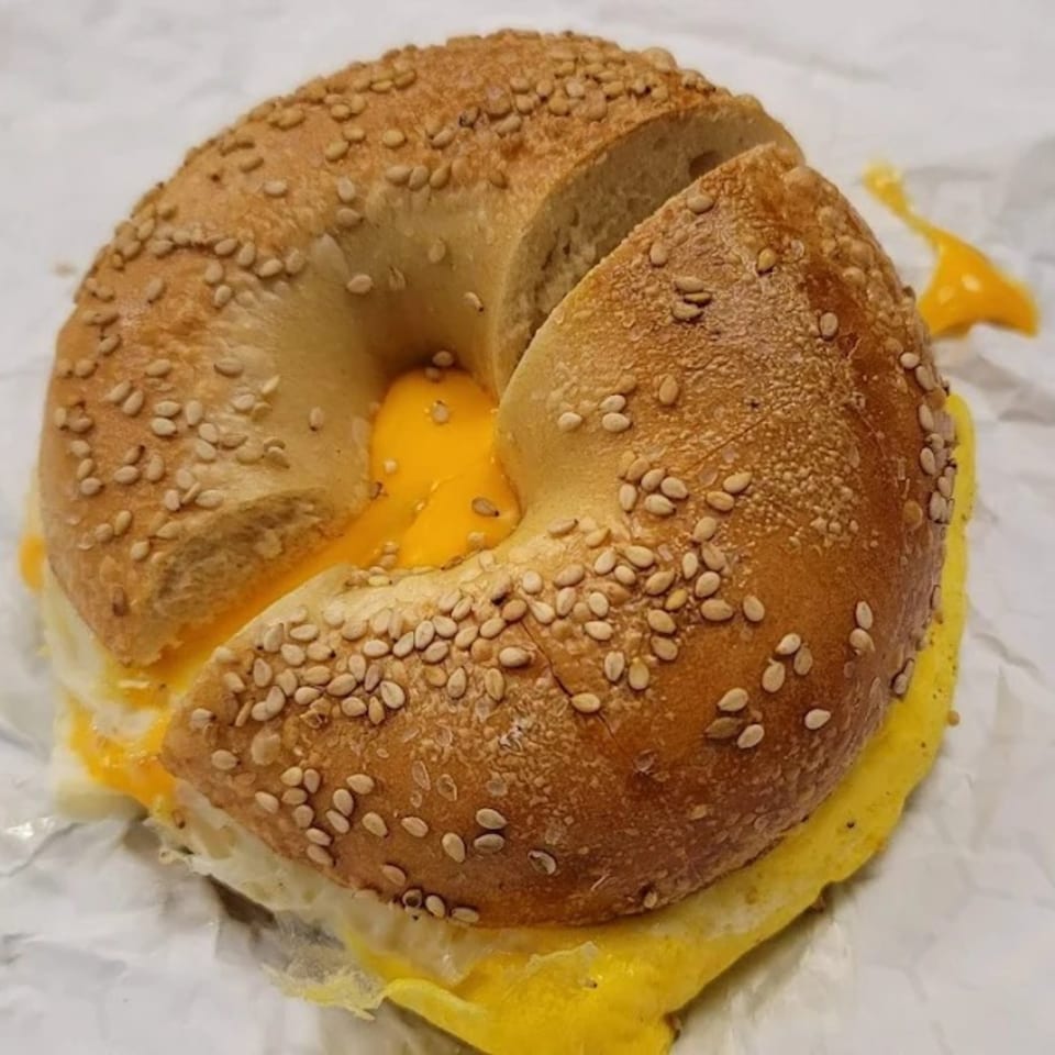 A sesame bagel from The Bagel Club, sliced open with a fried egg and melted cheese inside.